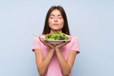 Izole mavi arka plan üzerinde salata ile genç kadın