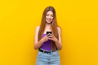 Sarı arka plan izole edilmiş genç bir kadın cep telefonuyla mesaj gönderiyor.