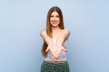 İzole edilmiş mavi arka plan üzerinde genç bir kadın bir ilan vermek için avucunun içinde hayali bir alan tutuyor.