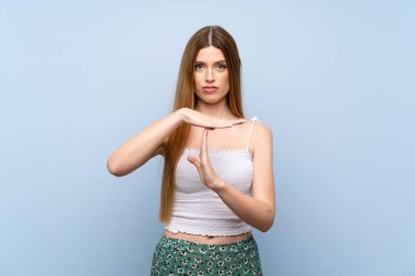 Soyutlanmış mavi arka planda genç bir kadın zaman aşımı hareketi yapıyor.