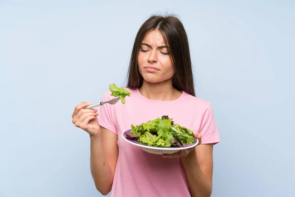 Young woman with salad over isolated blue background