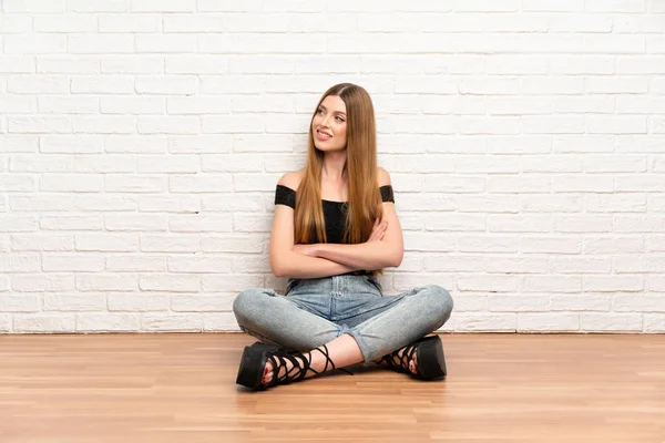 Genç bir kadın yerde oturuyor, yan tarafa bakıyor.