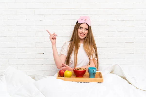 Young woman in dressing gown with breakfast pointing finger to the side