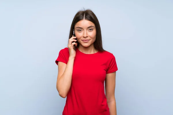 Brunette young woman with a mobile phone over isolated blue wall — Stock Photo, Image