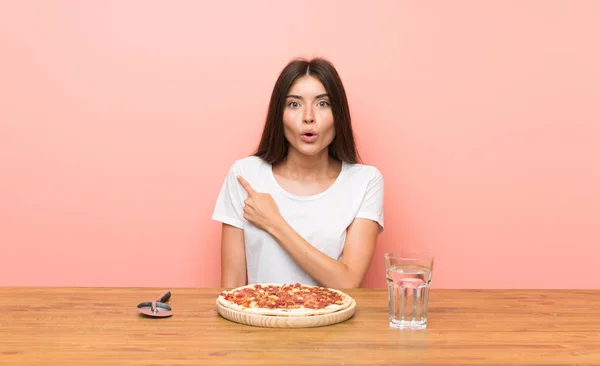 Young woman with a pizza surprised and pointing side
