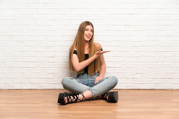 Genç bir kadın yerde oturuyor. Davet edildiği için ellerini yana açıyor.