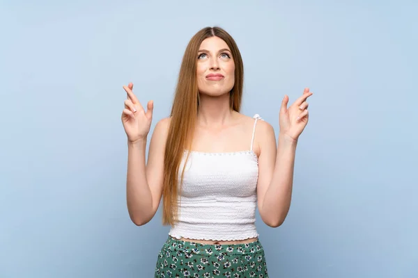 Young woman over isolated blue background with fingers crossing and wishing the best