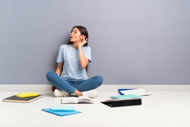 Yerde bir şeyler dinleyerek birçok kitap ile genç öğrenci kadın