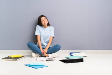 Yerde gülen ve yukarı bakan birçok kitap ile genç öğrenci kadın