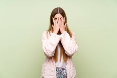 Gözleri kaplayan ve parmaklardan bakan yeşil duvar üzerinde sabahlık genç kadın