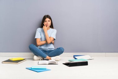 Yerde birçok kitap ile genç öğrenci kadın bir fikir düşünme