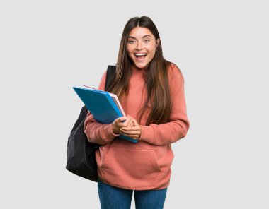 İzole gri arka plan üzerinde sürpriz yüz ifadesi ile defter tutan genç öğrenci kadın