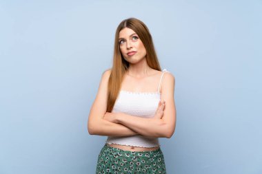 Soyutlanmış mavi arka planda genç bir kadın omuzlarını kaldırırken şüpheyle hareket ediyor.