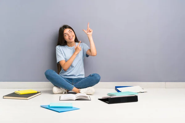 Young student woman with many books on the floor pointing with the index finger a great idea