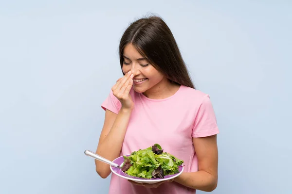 Young woman with salad over isolated blue background smiling a lot