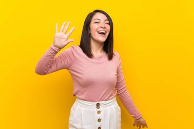 Izole sarı arka plan üzerinde genç Meksikalı kadın mutlu ifade ile el ile selamlama