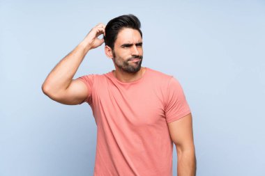 Başını çizerken şüpheleri olan izole mavi arka plan üzerinde pembe gömlek yakışıklı genç adam