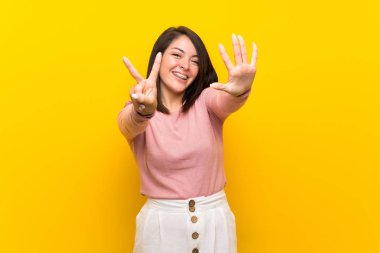 Izole sarı arka plan üzerinde genç Meksikalı kadın parmakları ile yedi sayma