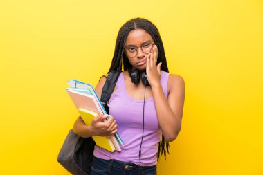 Izole sarı duvar üzerinde uzun örgülü saçları ile Afrikalı-Amerikalı genç öğrenci kız mutsuz ve sinirli