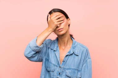 İzole edilmiş pembe arka planı olan genç bir kadın elleriyle gözlerini kapatıyor.