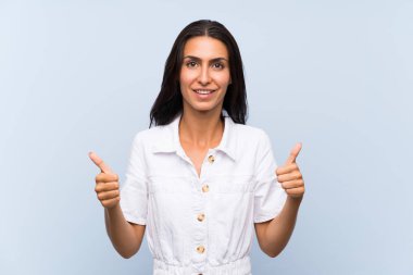 Soyutlanmış mavi arka planda genç bir kadın baş parmak işareti yapıyor.