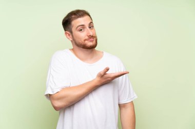 Yeşil arka plan üzerinde Yakışıklı adam gelmeye davet için yan ellerini uzatan