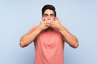 Elleri ile ağız kapsayan izole mavi arka plan üzerinde pembe gömlek yakışıklı genç adam