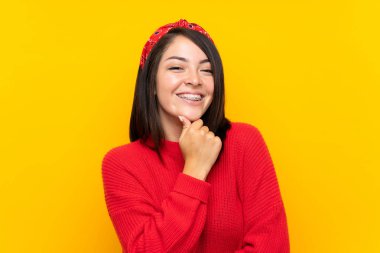 Sarı duvar üzerinde kırmızı kazak ile genç Meksikalı kadın gülüyor