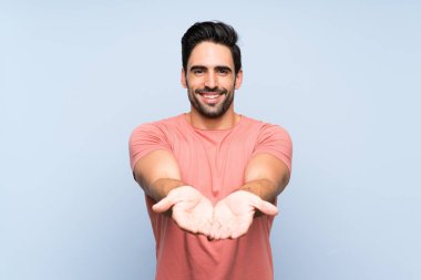 Bir reklam eklemek için avuç üzerinde copyspace hayali tutan izole mavi arka plan üzerinde pembe gömlek yakışıklı genç adam