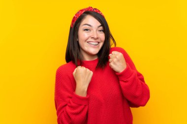 Bir zaferi kutlayan sarı duvar üzerinde kırmızı kazak ile genç Meksikalı kadın