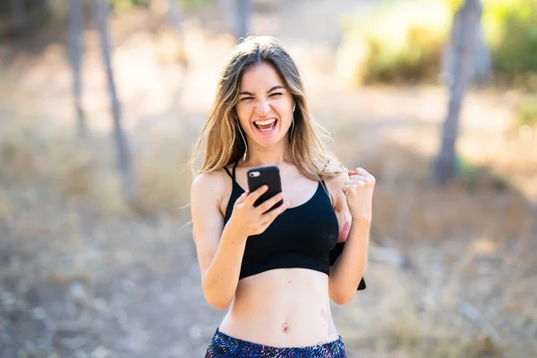 Young sport girl at outdoors with phone in victory position