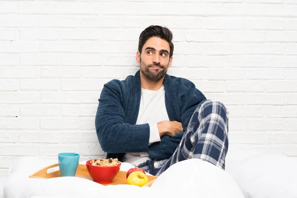 Hombre Cama Con Bata Desayunando Haciendo Gestos Dudas Mientras Levanta —  Fotos de Stock