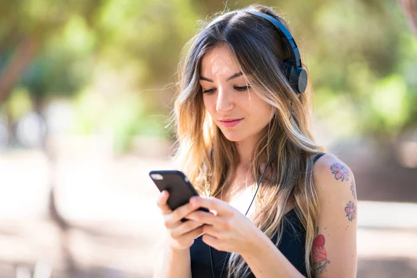 Młoda Dziewczyna Zewnątrz Parku Słuchania Muzyki Telefonu Komórkowego — Zdjęcie stockowe