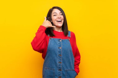 Telefon jesti yapan sarı duvar üzerinde tulum ile genç Meksikalı kadın. Beni geri arayın işareti