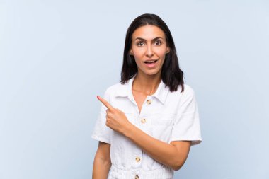 İzole edilmiş mavi arka planda genç bir kadın, parmağını yana doğru gösteriyor.