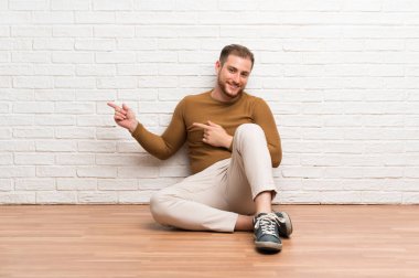 Yerde oturan sarışın adam tarafına parmak işaret