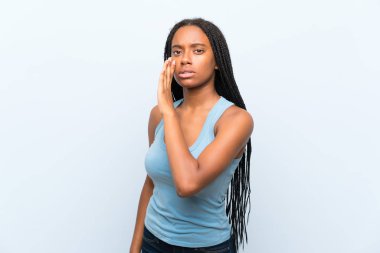 Izole mavi arka plan üzerinde uzun örgülü saçları ile Afrikalı-Amerikalı genç kız bir şey fısıldıyor