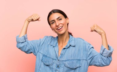 Soyutlanmış pembe arka plan zaferi kutlayan genç bir kadın.