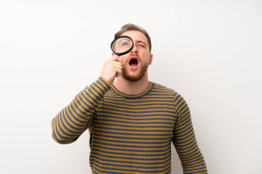 Bir büyüteç tutan izole beyaz duvar üzerinde Yakışıklı adam