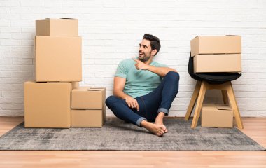 Yakışıklı genç adam yan parmak işaret kutuları arasında yeni bir evde hareket