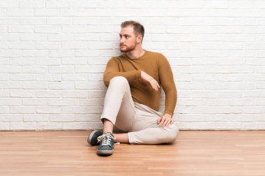 Sarışın adam yan bakarak katta oturan