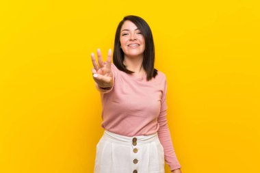 Izole sarı arka plan üzerinde Genç Meksikalı kadın mutlu ve parmakları ile üç sayma