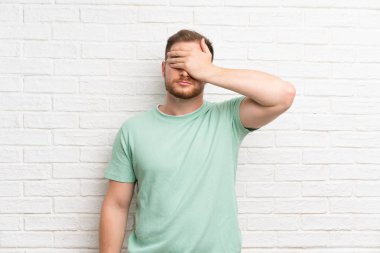 Elleriyle gözleri kaplayan tuğla duvar üzerinde Sarışın adam