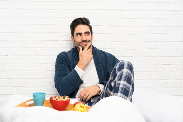 Man in bed with dressing gown and having breakfast thinking an idea