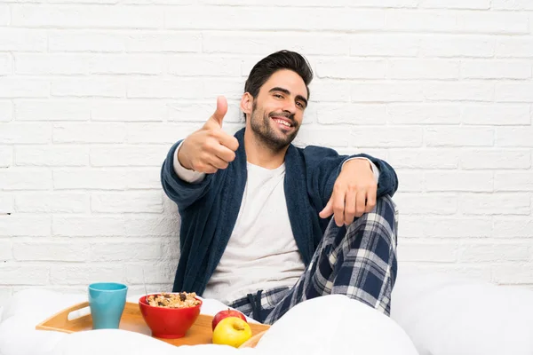 Man in bed with dressing gown and having breakfast with thumbs up because something good has happened