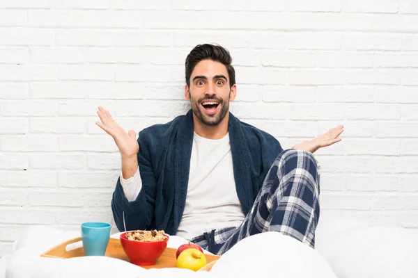 Man in bed with dressing gown and having breakfast with shocked facial expression