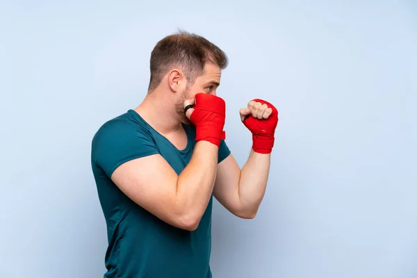 Blonde sport man over blue wall in boxing bandages — Stock Photo, Image