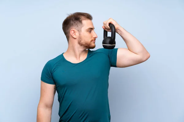 Hombre deportivo rubio sobre pared azul con kettlebell — Foto de Stock