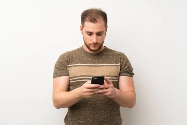 Pohledný Muž Přes Izolovanou Bílou Zeď Používající Mobilní Telefon — Stock fotografie