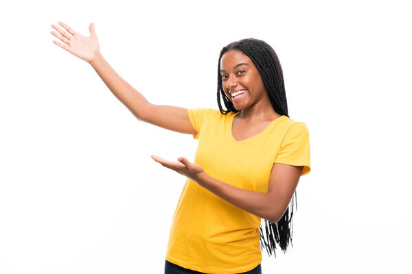 Афроамериканская девочка-подросток с длинными плетеными волосами на изолированном белом фоне протягивает руки в сторону для приглашения прийти
